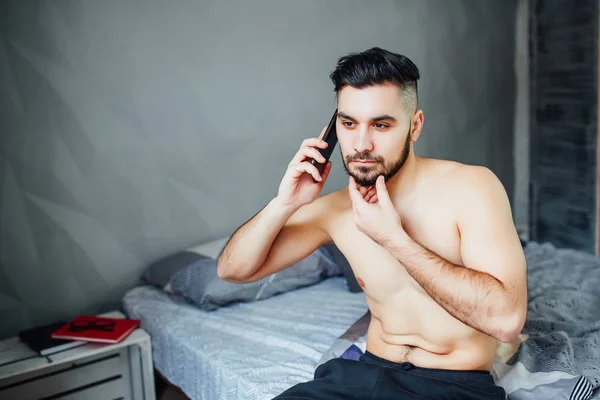 Junger Mann Sitzt Auf Bett Und Telefoniert Mit Smartphone — Stockfoto