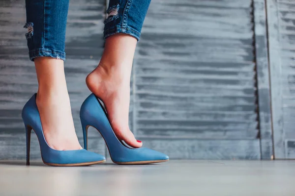 Woman in blue jeans and blue high heels on grey background
