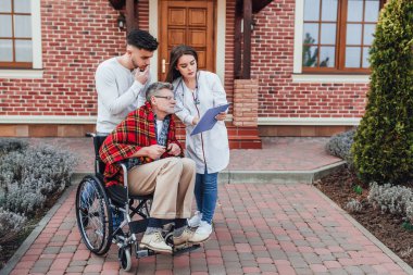 Hemşire ile Oğlu tekerlekli sandalyede yaşlı adam hakkında konuşuyor ve sonuçları bakıyor