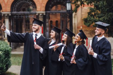 Diploma tutan ve telefonda selfie yapan çok ırklı mezunların portresi