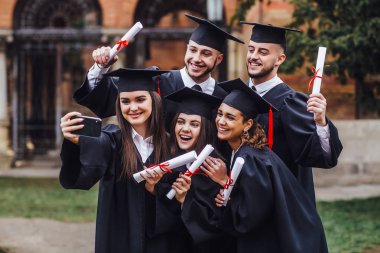 Diploma tutan ve telefonda selfie yapan çok ırklı mezunların portresi