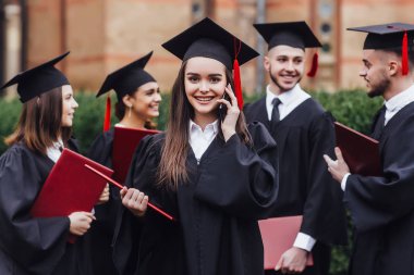 Elinde kırmızı diplomayla genç ve çekici bir kadın telefonda konuşuyor.