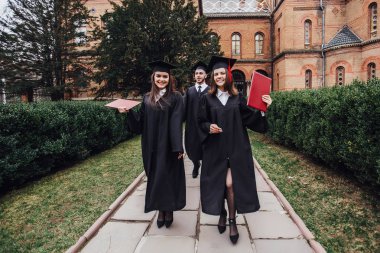 Üniversite bahçesinde yürüyen diplomalı başarılı mezunlar