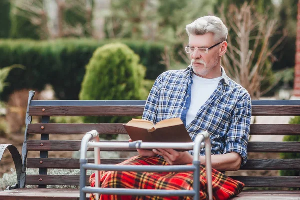 Old man reading book while siting at garden near clinic