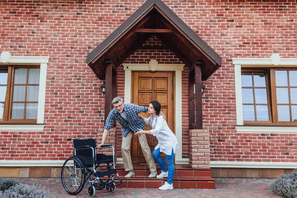 Медсестра Помогает Мужчине Сидящему Инвалидной Коляске Рядом Домом Престарелых — стоковое фото