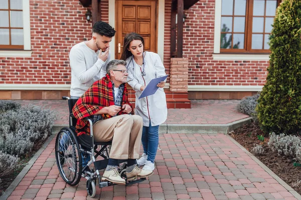 Hemşire ile Oğlu tekerlekli sandalyede yaşlı adam hakkında konuşuyor ve sonuçları bakıyor