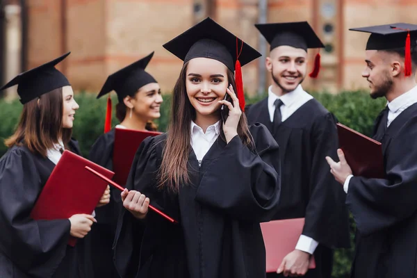Young attractive woman master with red diploma in hand speaking by phone