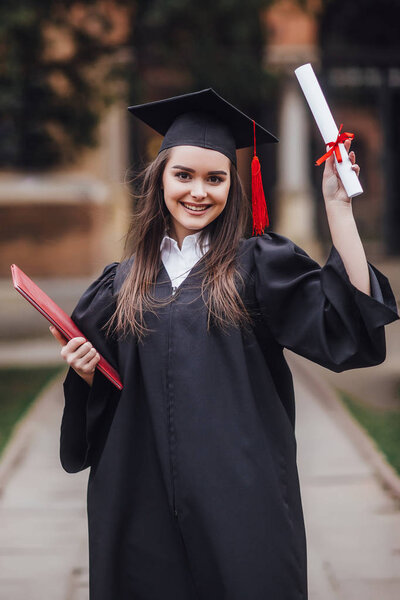 Smiling woman with degree looking at camera near university