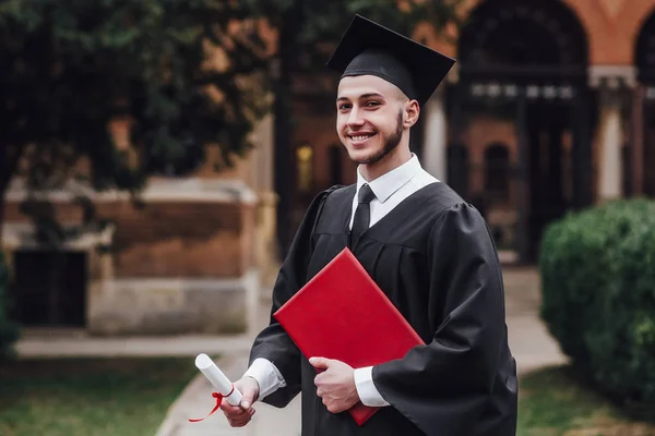 Νέος Όμορφος Αποφοίτησε Μανδύα Κρατώντας Πτυχίο Κοντά Στο Πανεπιστήμιο — Φωτογραφία Αρχείου