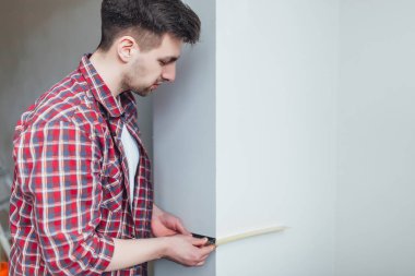 young man holding ruler, belt hanging tools and measure wall