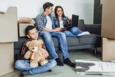 dizüstü bilgisayar kullanarak anne ve baba yakınında katta oturan oyuncak ayı ile çocuk