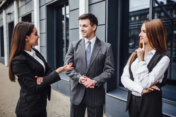 Three cheerful young business people talking to each other while walking outdoors