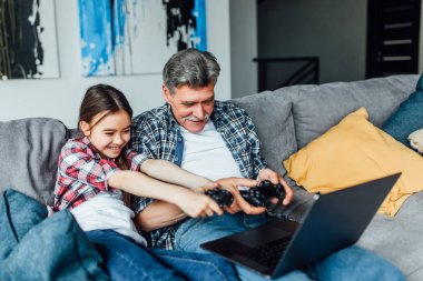 Büyükbaba ve torunu joysticks tutarak ve modern dizüstü bilgisayarda oyun oynuyor