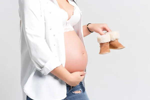 白い背景に隔離された赤ちゃんのための白い靴のペアを保持している妊娠中の女性 — ストック写真