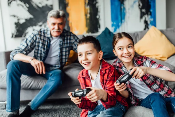 Niño Niña Jugando Consola Juegos Sonriendo Mientras Abuelo Sentado Sofá —  Fotos de Stock