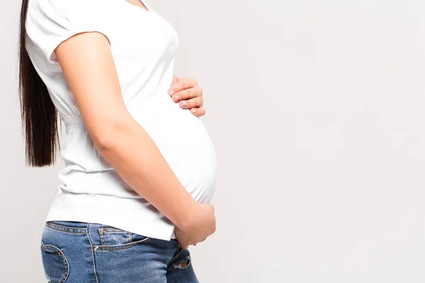 白い背景に隔離されたおなかの上に手を持つ妊娠中の女性 — ストック写真