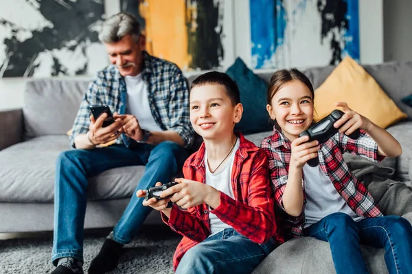 Niño Niña Jugando Consola Juegos Sonriendo Mientras Abuelo Usa Teléfono —  Fotos de Stock