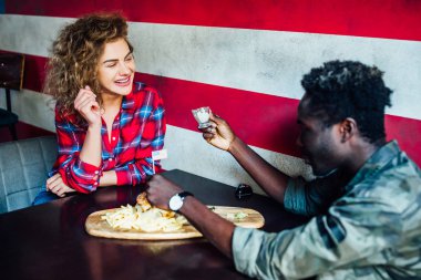 Kadın bir erkekle barda dinleniyor, konuşuyor, gülüyor, fast food yiyor.