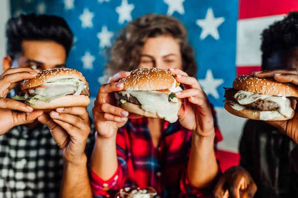 happy friends eating burgers in bar together, selective focus