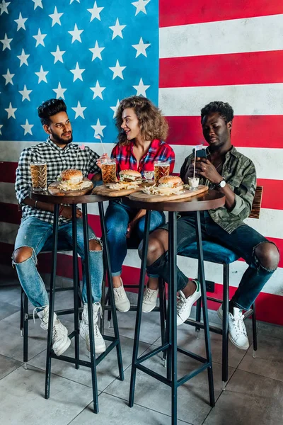 Young best friends laughing and talking while eating burgers and beer