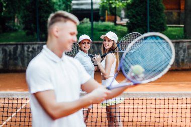 Arkasında iki kız ile tenis raket sallanan adam 