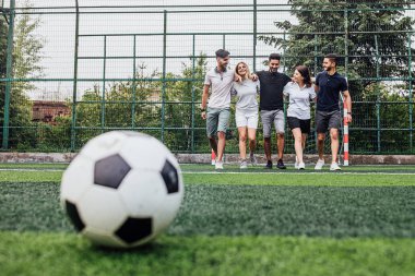 arkadaşlar birbirlerine sarılma ve futbol sahasında yürüyüş, ön planda topu