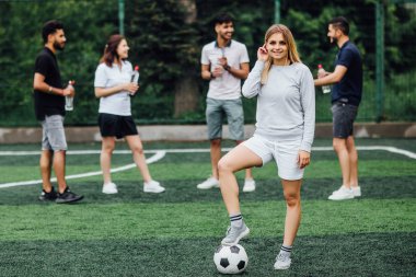sahada arkadaşlar, ön planda futbol topu ile genç kadın