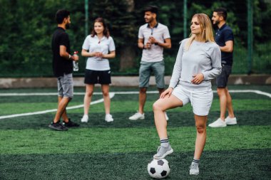 sahada arkadaşlar, ön planda futbol topu ile genç kadın
