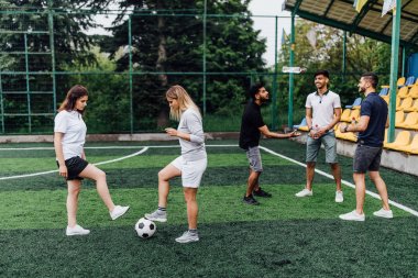 stadyumda futbol oynayan arkadaşlar, ön planda topu ile kadınlar