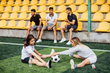 stadyumda futbol oynayan arkadaşlar, ön planda topu ile kadınlar