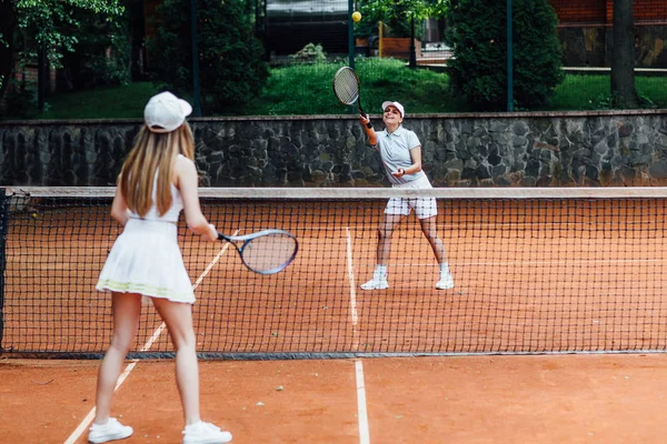 Eğitim sırasında şapkalı iki güzel kadın ve tenis üniforması tenis topu servisi 