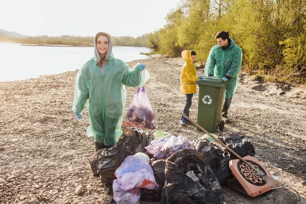 group of volunteers with garbage bags cleaning area near lake