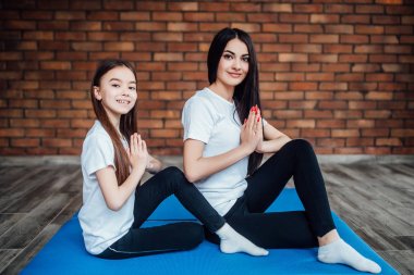 Küçük kızı olan genç bir kadın evde yoga yaparken gülümsüyor.