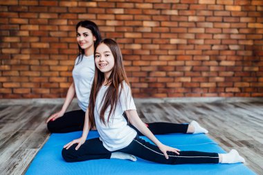 Mavi yoga minderi üzerinde sabah egzersizi yapan kızı olan bir kadın.