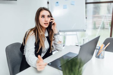 Güzel iş kadını telefonda konuşuyor ve dizüstü bilgisayar kullanıyor 