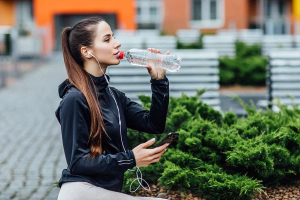 Pretty woman in sport wear, drinking water on fresh air after morning running. Healthy concept.