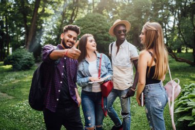 Dört neşeli arkadaş grubu, öğrenciler parkta birlikte vakit geçirmek, sarılma, kameraya bakarak.
