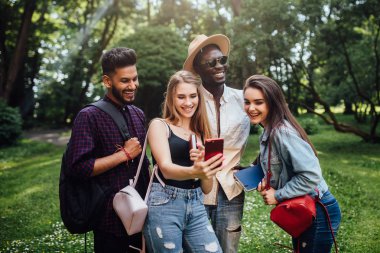 Dört neşeli arkadaş grubu, öğrenciler parkta birlikte vakit geçirmek, kameralı telefon bakarak, dersten sonra dinlenmek.
