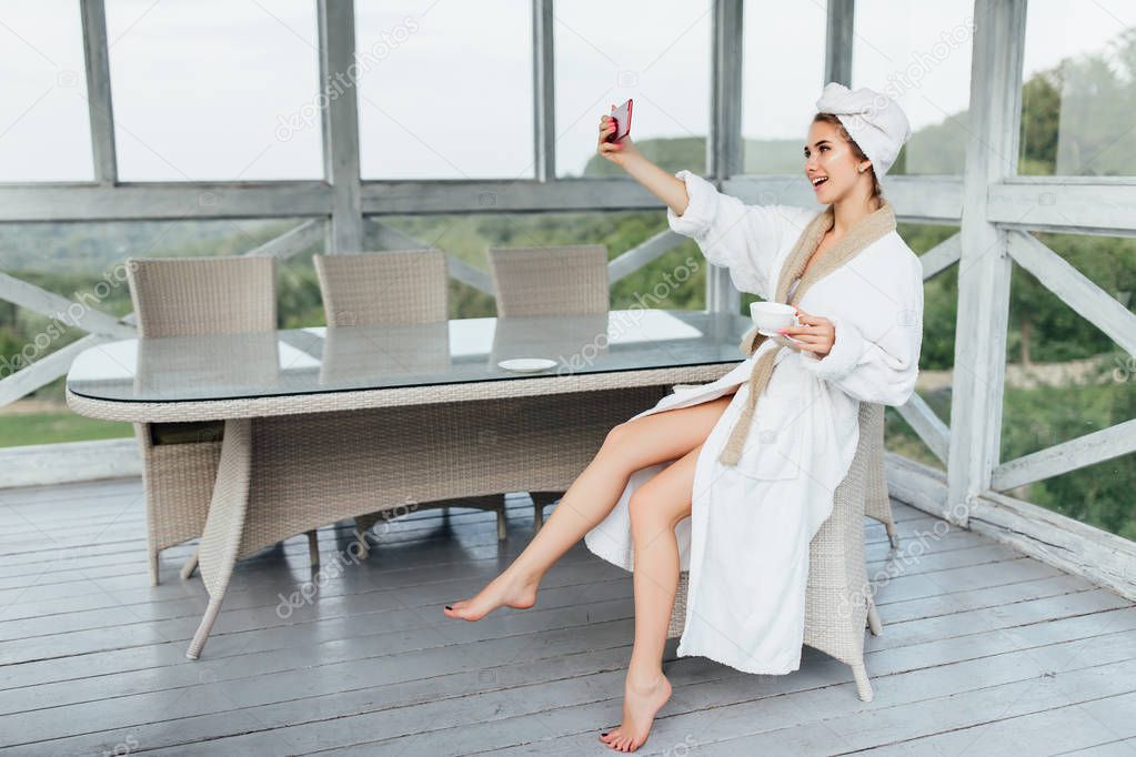 Selfie time. Gorgeous woman in white robe, resting in summer terrace on luxury hotel.