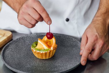 Fotoğrafı kapat. Aşçı mutfakta meyveli kek ve şeker süslüyor. Pasta, aşçılık, aşçılık, fırın, yemek ve insan konsepti dekore ediyor..