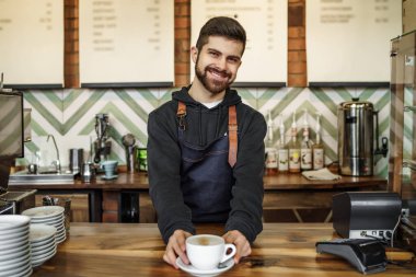Yakışıklı genç barmen tezgahın yanında duruyor, müşteri için taze ve sıcak kahve tutuyor..