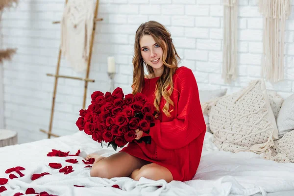 Güzel sarışın kadın elinde bir buket kırmızı gülle kameraya poz veriyor.