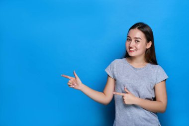 Genç ve güzel Asyalı gülümsüyor ve mavi arka planı işaret ediyor..