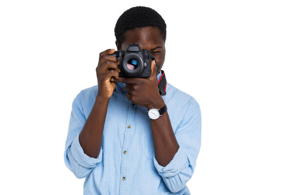 Young african male photographer focuses with professional DSLR camera on isolated white background.