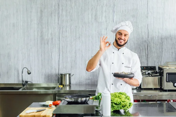 Portrait of the chef in the kitchen of the restaurant with a ready made dish on his hands.