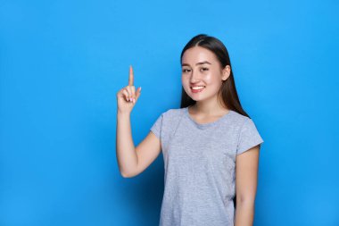 Genç, güzel Asyalı gülümseyen ve mavi arka planda baş parmağını gösteren.