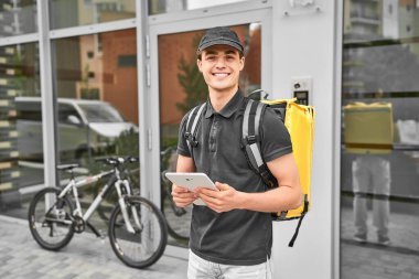 Evdeki teslimatçının portresi üniformalı, sırt çantası ve tabletli..