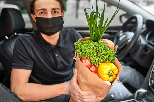 Delivery man in protective mask holds bag with fresh vegetables, delivery from the store around the town. Close up.