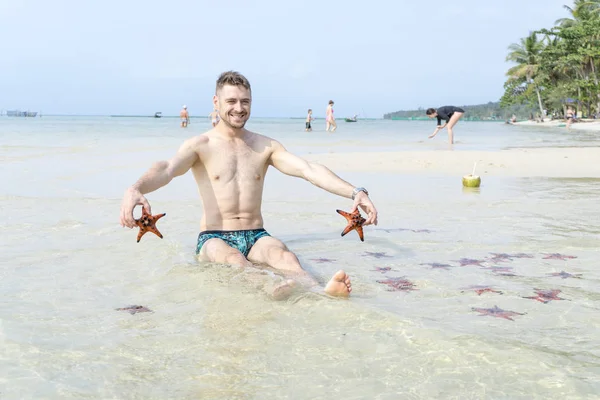 Seyahat oğlan kırmızı starfishes yapar komik fotoğraflar Phu Quoc Adası kristal berraklığında su ile denizde oturuyor