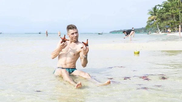 Seyahat oğlan kırmızı starfishes yapar komik fotoğraflar Phu Quoc Adası kristal berraklığında su ile denizde oturuyor